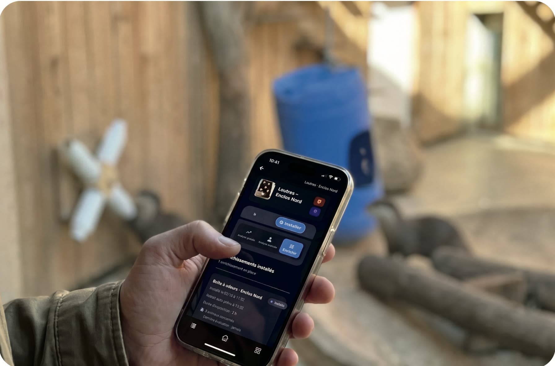 Un soigneur consulte les enrichissements installés dans l'application Animal Welfare Monitor, devant l'enclos des loutres